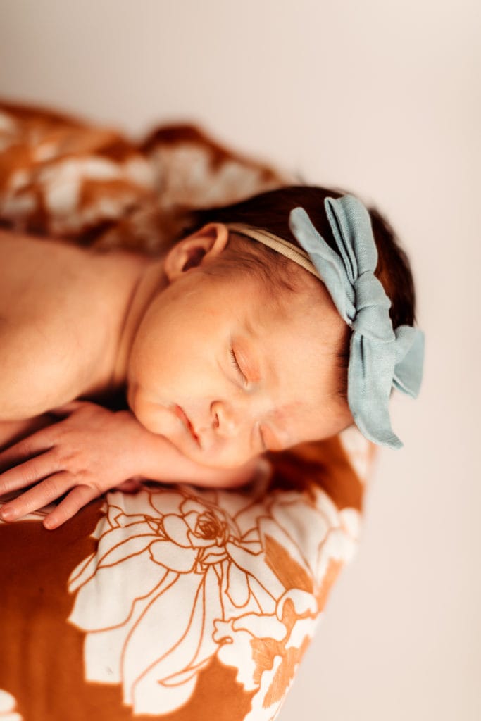 Family Photographer, a newborn baby lays cozily on a floral cushion